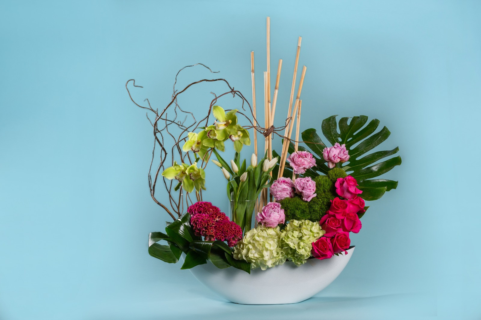 Buds floral arrangement with orchids, roses and branches on a pale aqua backdrop